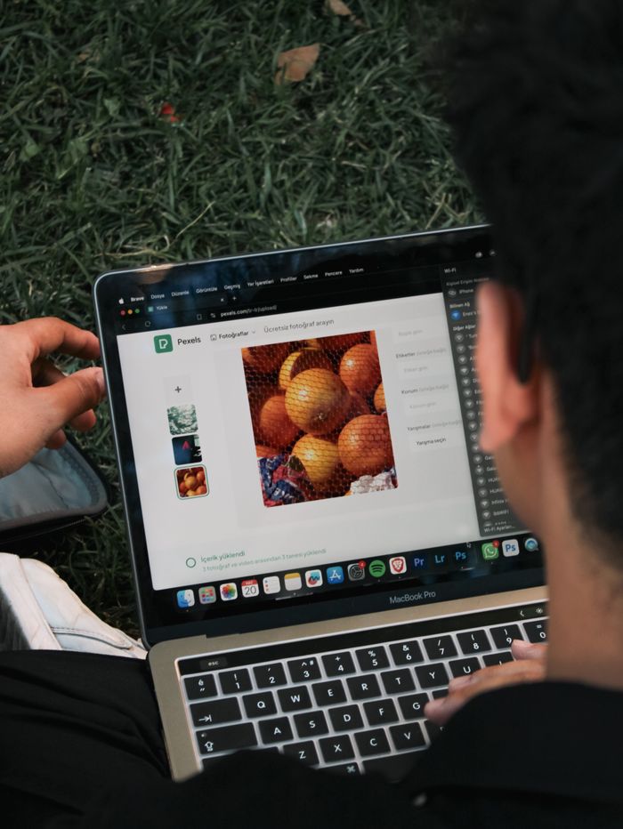 home-img A man edits a fruit image on a MacBook Pro while sitting outdoors on grass.